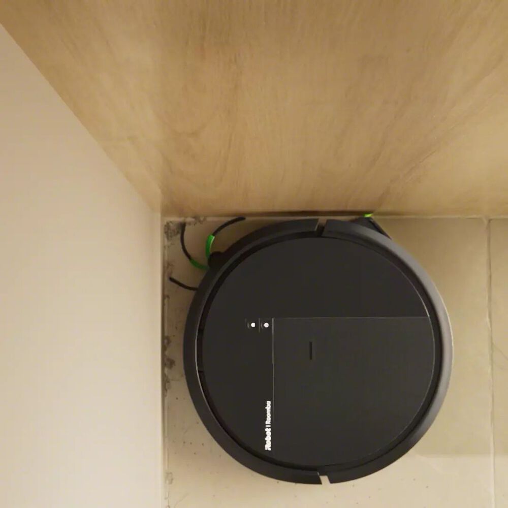 Roomba&reg; robot with a company design, vacuuming up dirt and dust in a tight corner.