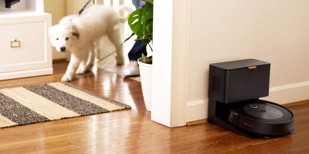 Een Roomba die wordt opgeladen terwijl er een hond door het huis beweegt